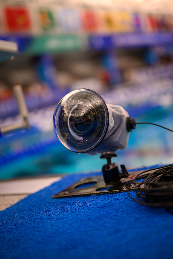 An Outex camera with dome lens and Flash, Data, or Tripod Add-on Kit is set poolside, aimed at the pool, with cables trailing beside it.