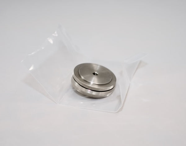 An Outex Accessories Miscellaneous Copy round metallic camera adaptor with a ridged edge rests on clear plastic against a white background.