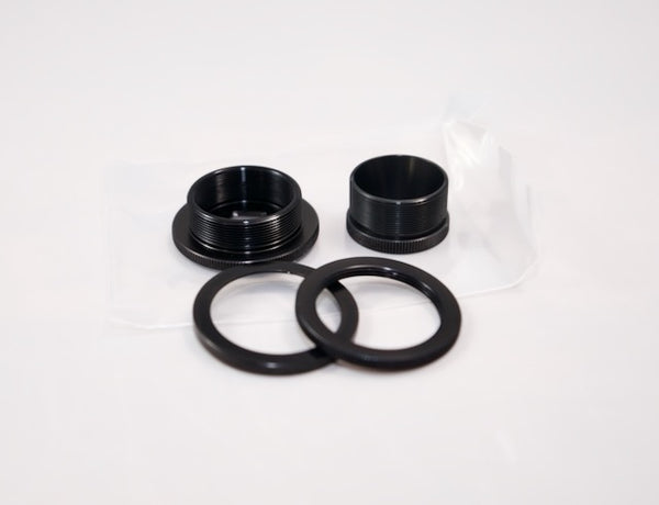 Two black metal threaded rings, two flat rings, and a small bag by Outex—ideal adaptors for tripods or cameras—on a white surface.