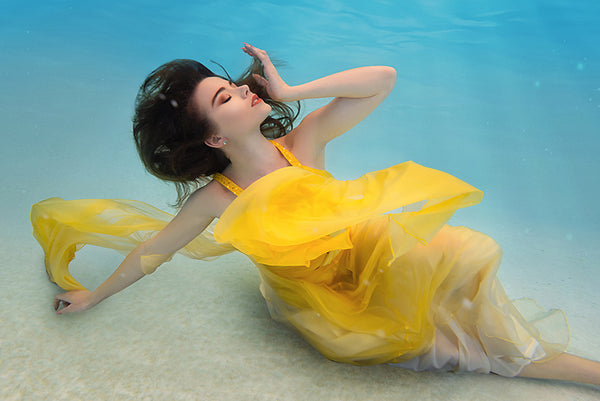 A woman with her arms spread in a yellow dress is inside a pool with blue water