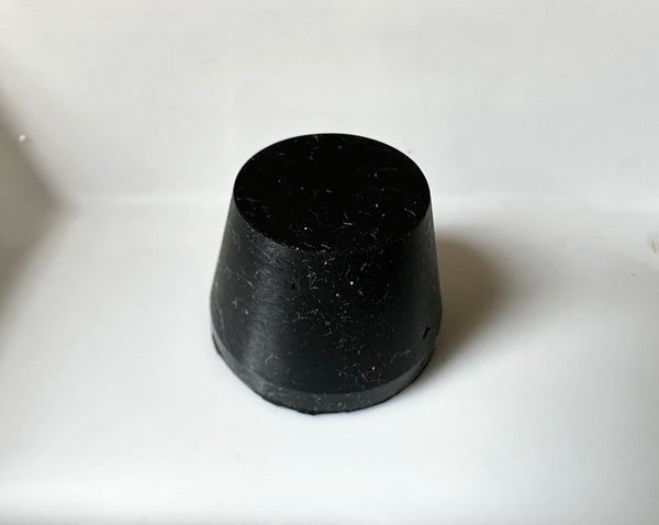 A black, cylindrical Outex rubber stopper from Accessories Miscellaneous sits on a white surface.
