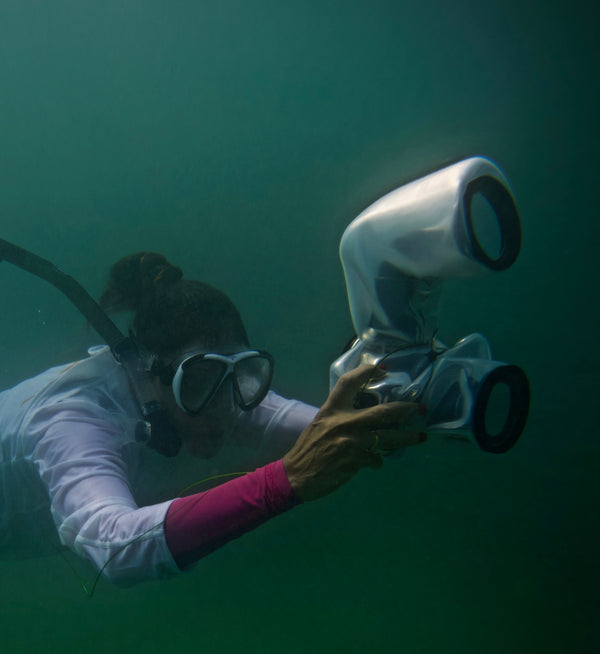 A scuba diver holds the Outex Flash Add-on Kit while swimming deep underwater, surrounded by greenish-blue water.