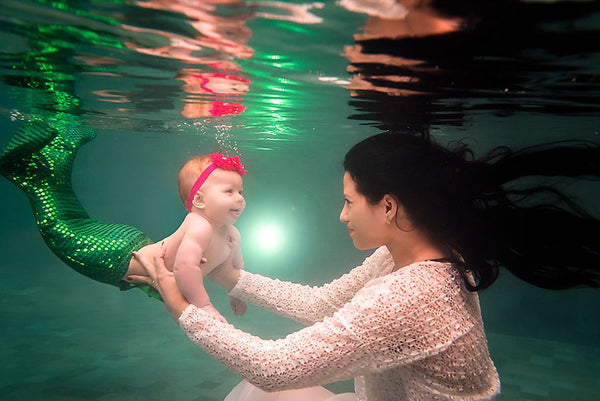 A woman and a baby dressed as a mermaid are underwater and laughing
