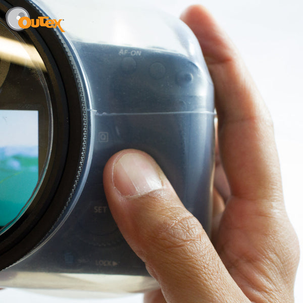 A hand presses a camera button inside the Outex Camera Pro Kit housing, with the Outex logo visible in the top left corner.