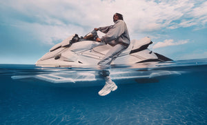 Split-level photograph of a rider on a white jet ski, with a white sneaker visible below the ocean surface.