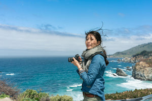 Outex AI assistant Nami holding a camera on a rocky blue coastline.