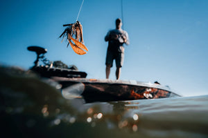 Fishing lure above the waterline with an angler standing on a bass boat in the background.