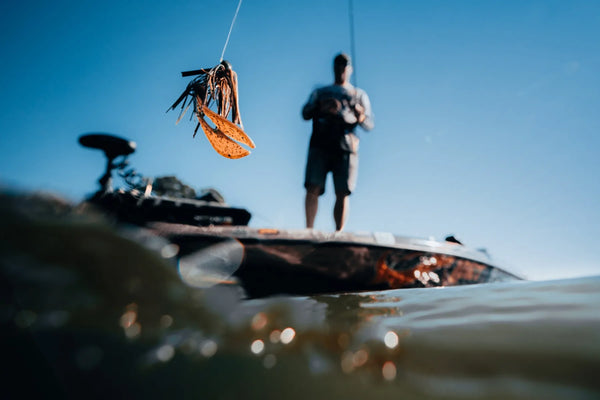 Fishing lure above the waterline with an angler standing on a bass boat in the background.
