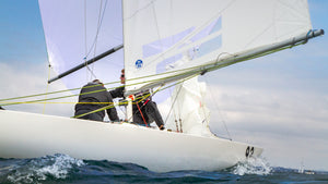Three people sailing a white sailboat on the water, adjusting ropes and sails under a partly cloudy sky.