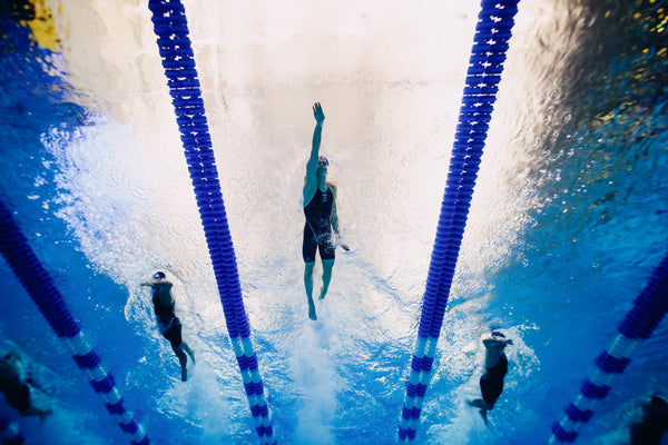 Underwater view of swimmers racing in a pool, one swimmer in the center reaching upward between lane dividers.