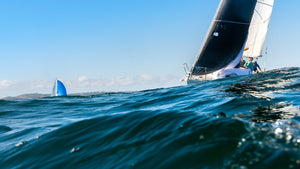 A sailboat leans into the wind on choppy blue water under a clear sky, with another boat visible in the distance.