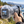 A GoPro Mission1 Pro ILS camera with an micro four-thirds lens inside a clear Outex Entry Kit waterproof housing against a blurred coastal background with ocean, rocks, and trees.