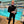 Photographer Finn O’Hara standing poolside in a Henderson wetsuit, holding a Canon R5 equipped with an RF 15-35mm lens inside a modular Outex underwater housing with a tethering cable attached