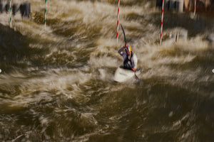A person in a kayak navigates through rough, fast-moving water and slalom gates during a whitewater kayaking course.