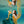 A woman with her arms spread in a green dress is underwater in a pool with blue water
