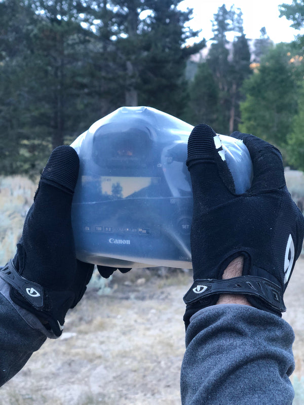 Hands with gloves holding a camera protected by an Outex case in the woods
