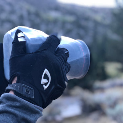 Hands with gloves holding a camera protected by an Outex case in the woods
