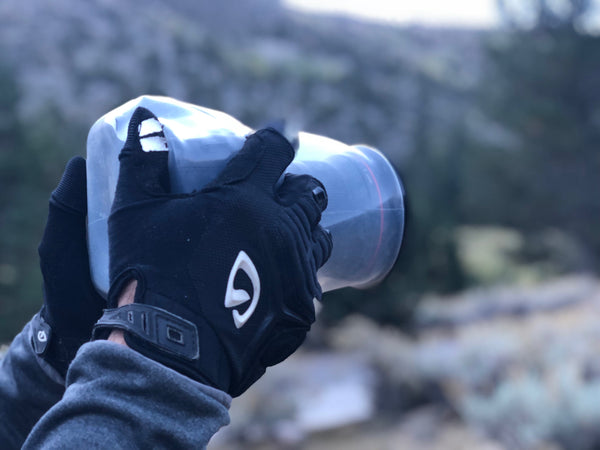 Hands with gloves holding a camera protected by an Outex case in the woods