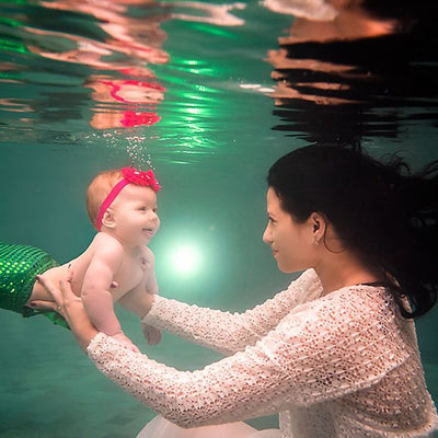 A woman and a baby dressed as a mermaid are underwater and laughing