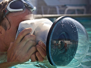 Man inside a swimming pool holding a camera that is protected by an Outex case and a big dome lens